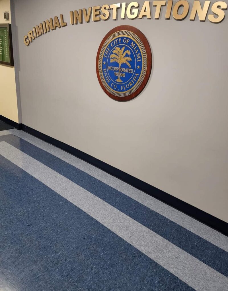 Wall with Criminal Investigations sign and a City of Miami seal, set against a blue and gray patterned floor, feels like the perfect backdrop for plotting mysterious computer repair mysteries. computer repair
