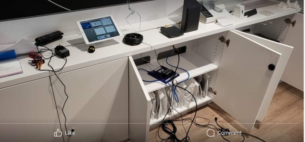 A tech setup with open cabinets displays networking equipment and cables. A tablet and remote rest on the counter amid plugged-in electronics, signifying a space primed for computer repair. Cables and cords visibly connect various devices, ready for diagnosis. computer repair